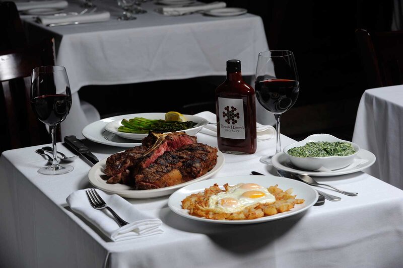 Plated eggs ontop of potatoes, plated steak with a side of vegetables and glass of red wine